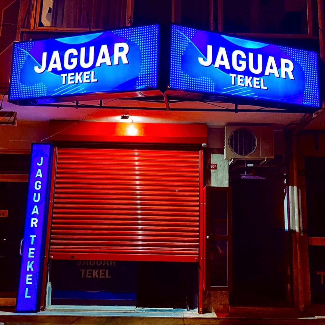 Jaguar Tekel’in mavi ışıklı tabelası ve kırmızı kepenkli dış cephesi